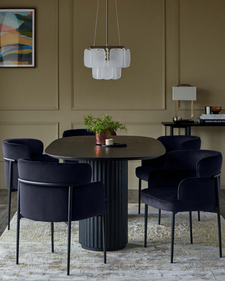 A dining set featuring a round dark oak table with a fluted pedestal base and four velvet upholstered chairs with black metal frames.