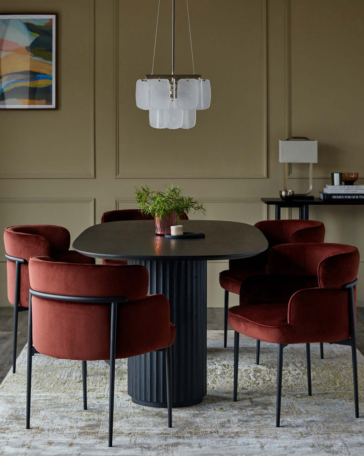Dining area with a round table, five rust-coloured velvet chairs, a modern pendant light, and abstract art.