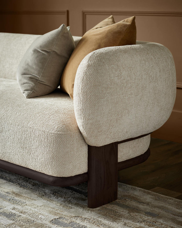 Beige sofa with rounded arm and bolster cushions in brown and beige, on a patterned rug.