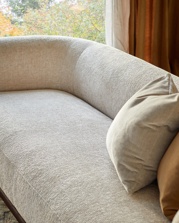 A modern, curved sofa with textured light-beige upholstery and soft pillows. A stylish piece for a contemporary living space.