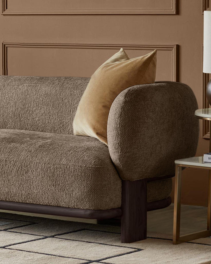 A modern brown fabric sofa with a neutral cushion, complemented by a marble top side table with brass legs.
