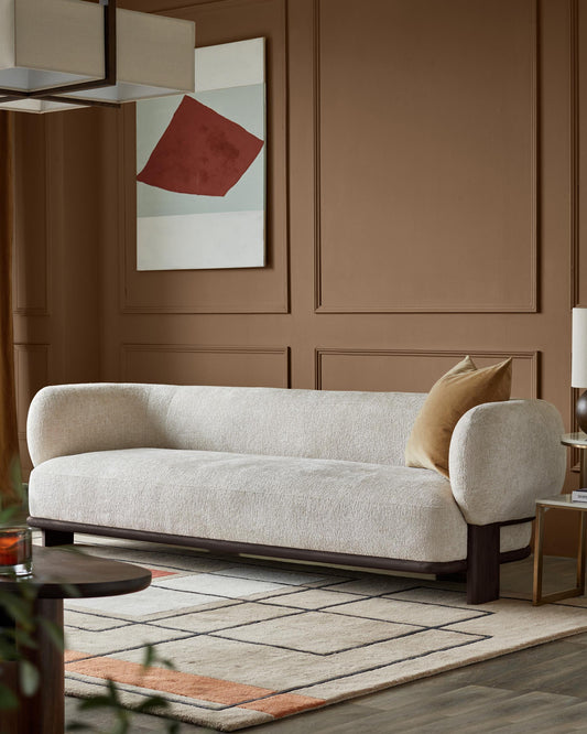 A contemporary cream sofa with a brown frame, paired with a geometric rug and brown accent wall.
