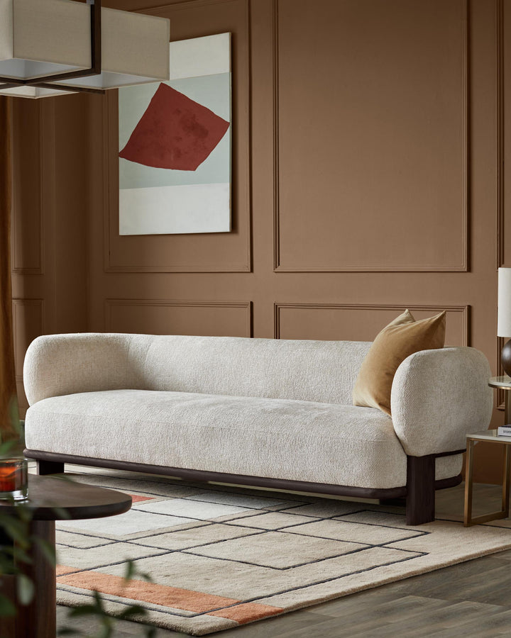 A contemporary cream sofa with a brown frame, paired with a geometric rug and brown accent wall.