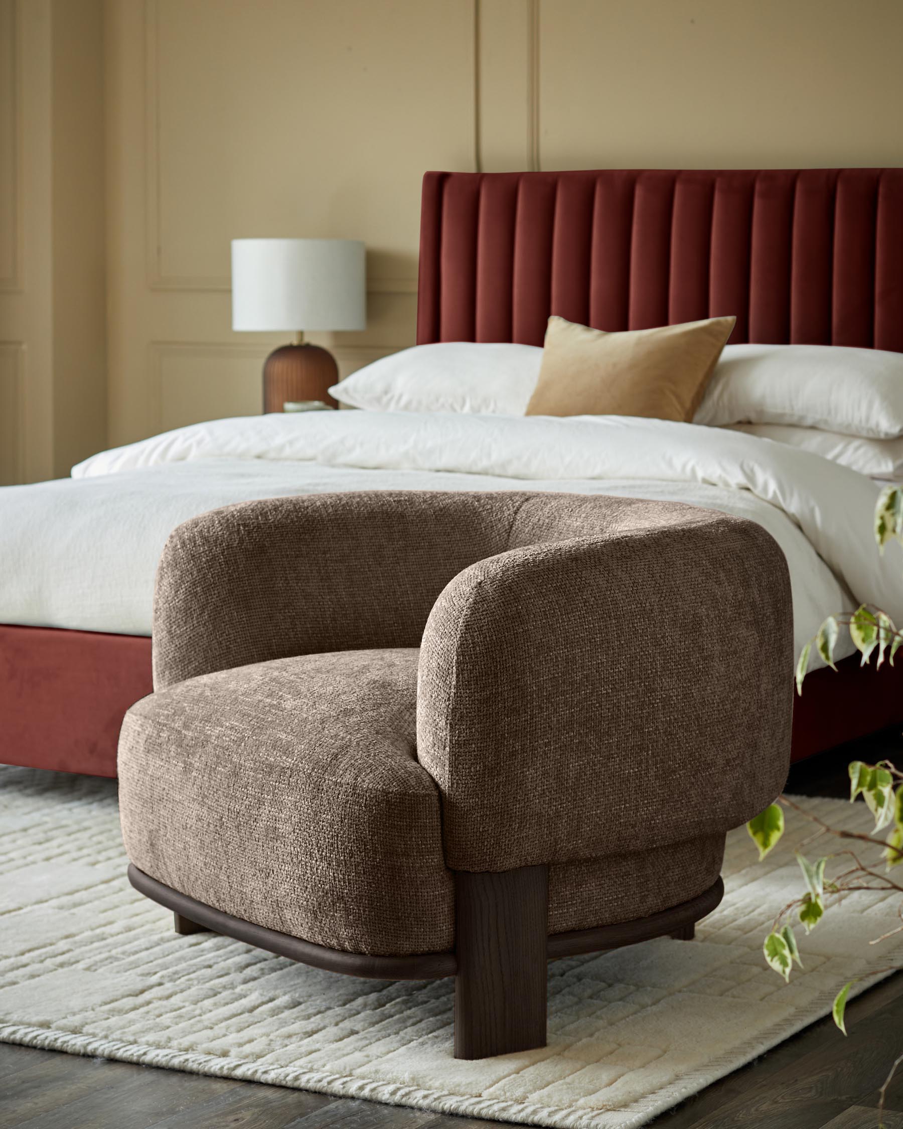 A cosy bedroom featuring an upholstered bed and a stylish brown armchair sat on a cream rug.