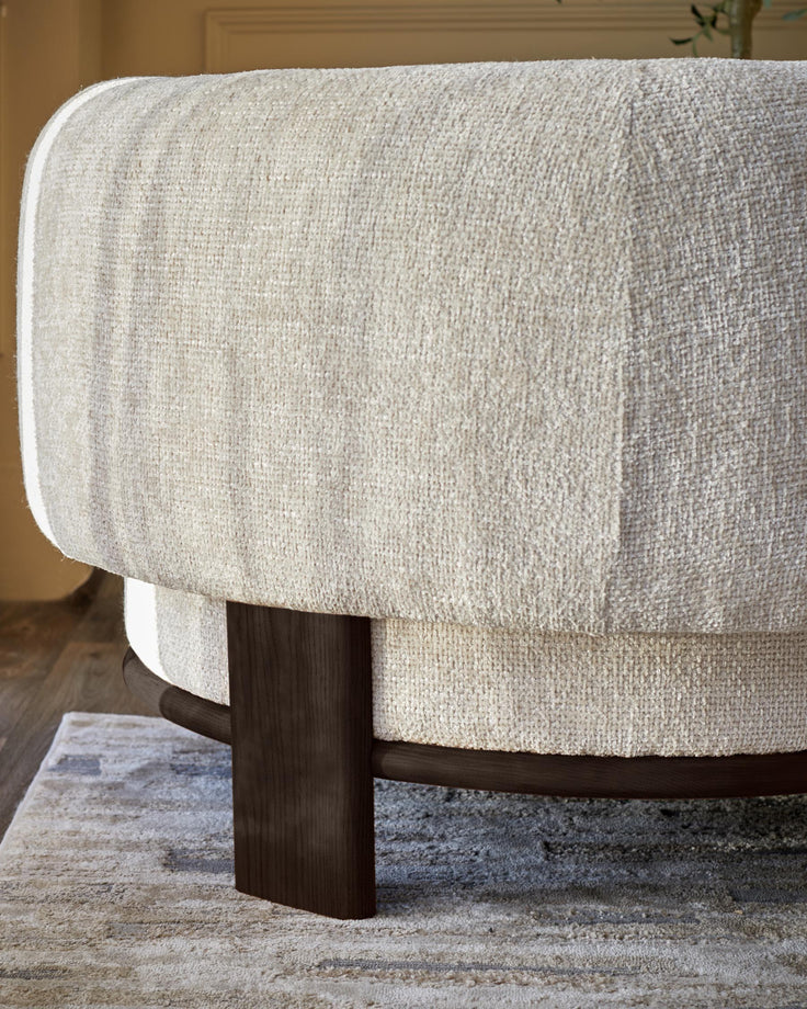 Close-up of a neutral-toned, textured fabric armchair with dark wooden legs, showcasing its modern design.