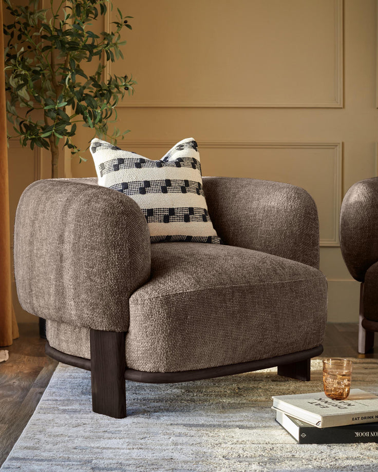A brown armchair with a cushion, placed on a patterned rug next to two books and a glass.