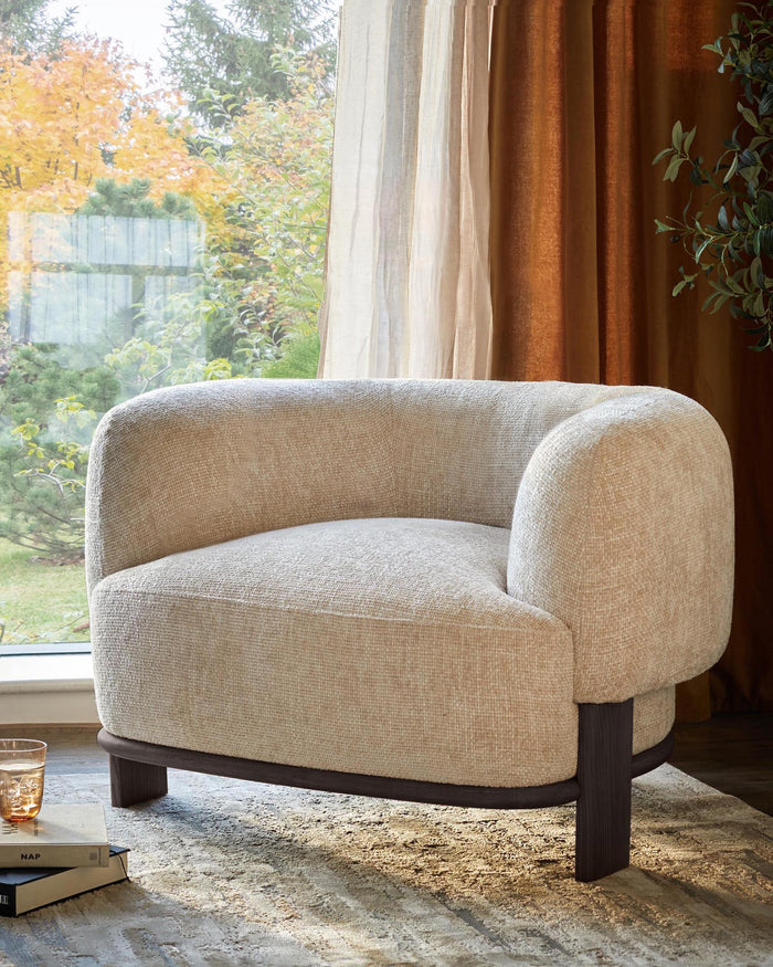 An inviting, neutral-toned armchair with dark wood legs, positioned near a sunlit window and draped curtains.