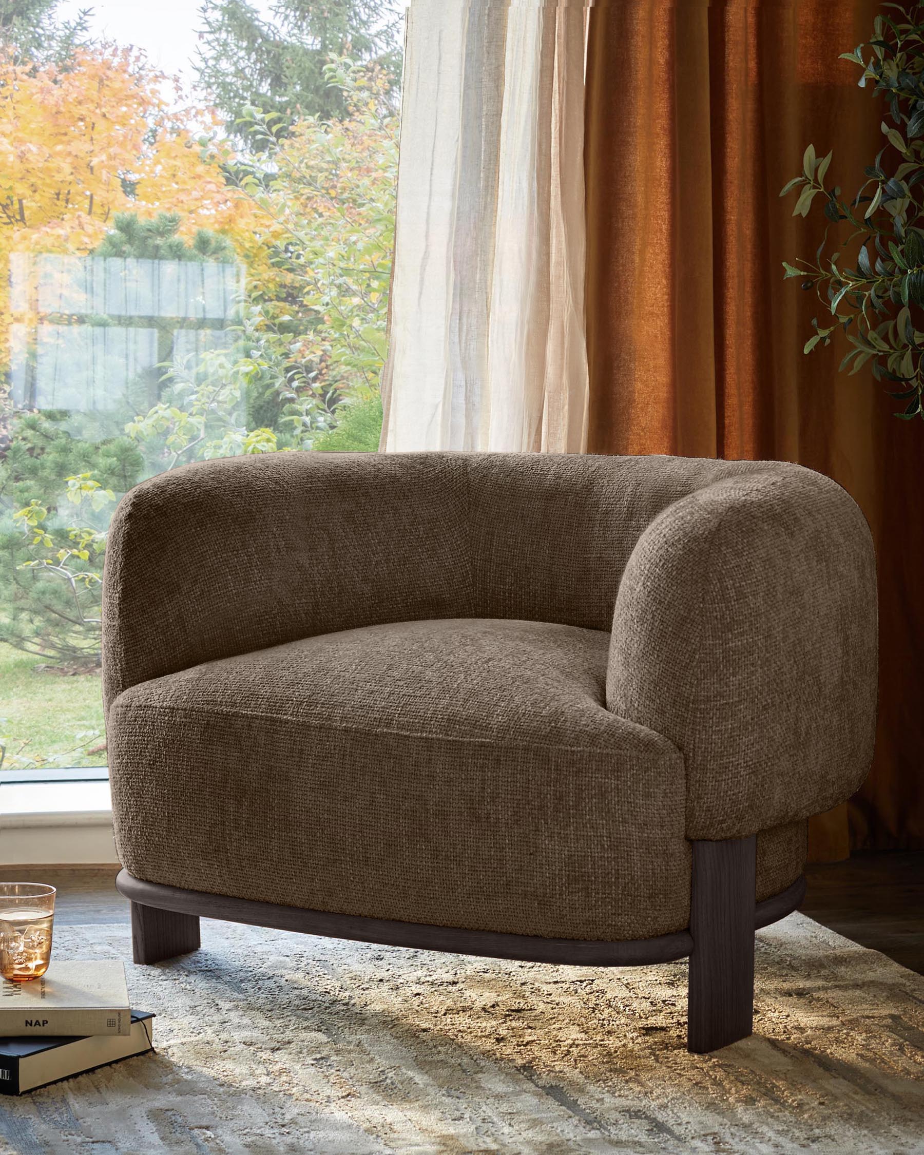 A modern brown armchair with dark wood legs sits on a patterned rug in front of a window with autumnal trees.