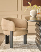Florence dining chair in honey fabric with black metal legs, shown in a styled room setting beside a round table.