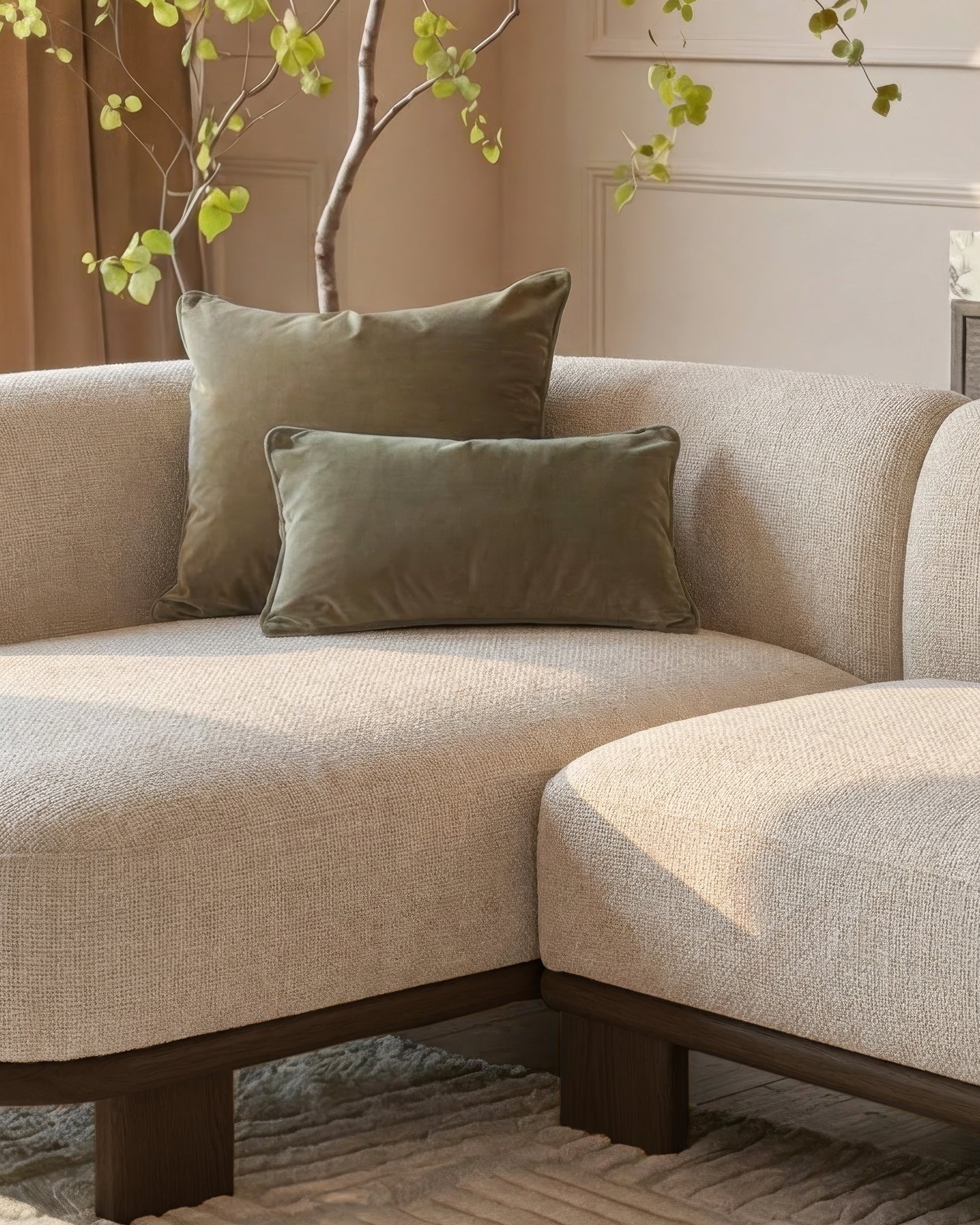 Florence left-hand-facing chaise sofa in natural fabric with dark wood base, styled with sage green pillows and decorative branch.