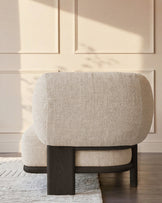 Cream fabric chaise lounge with curved backrest and dark wood frame, shown from rear angle in minimalist room setting.