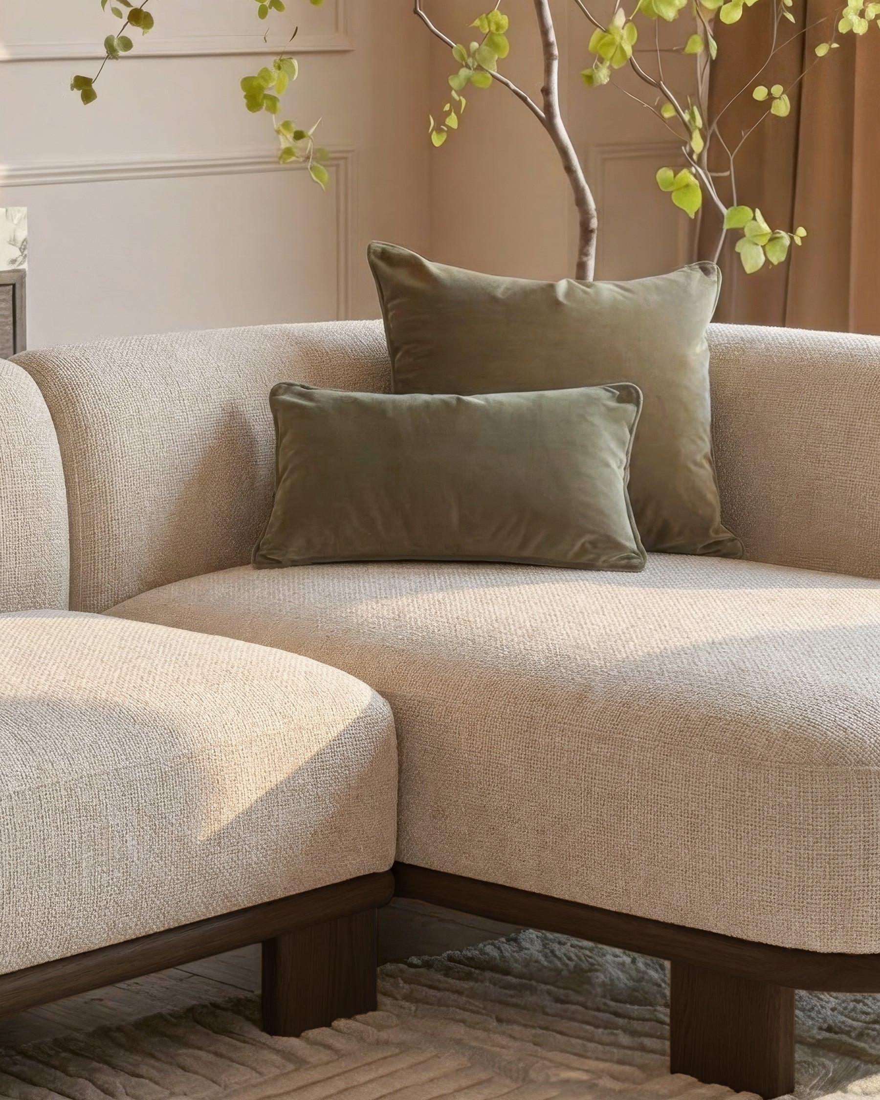 Florence right-hand facing chaise sofa in natural fabric with dark wood base, styled with olive pillows and decorative branch.