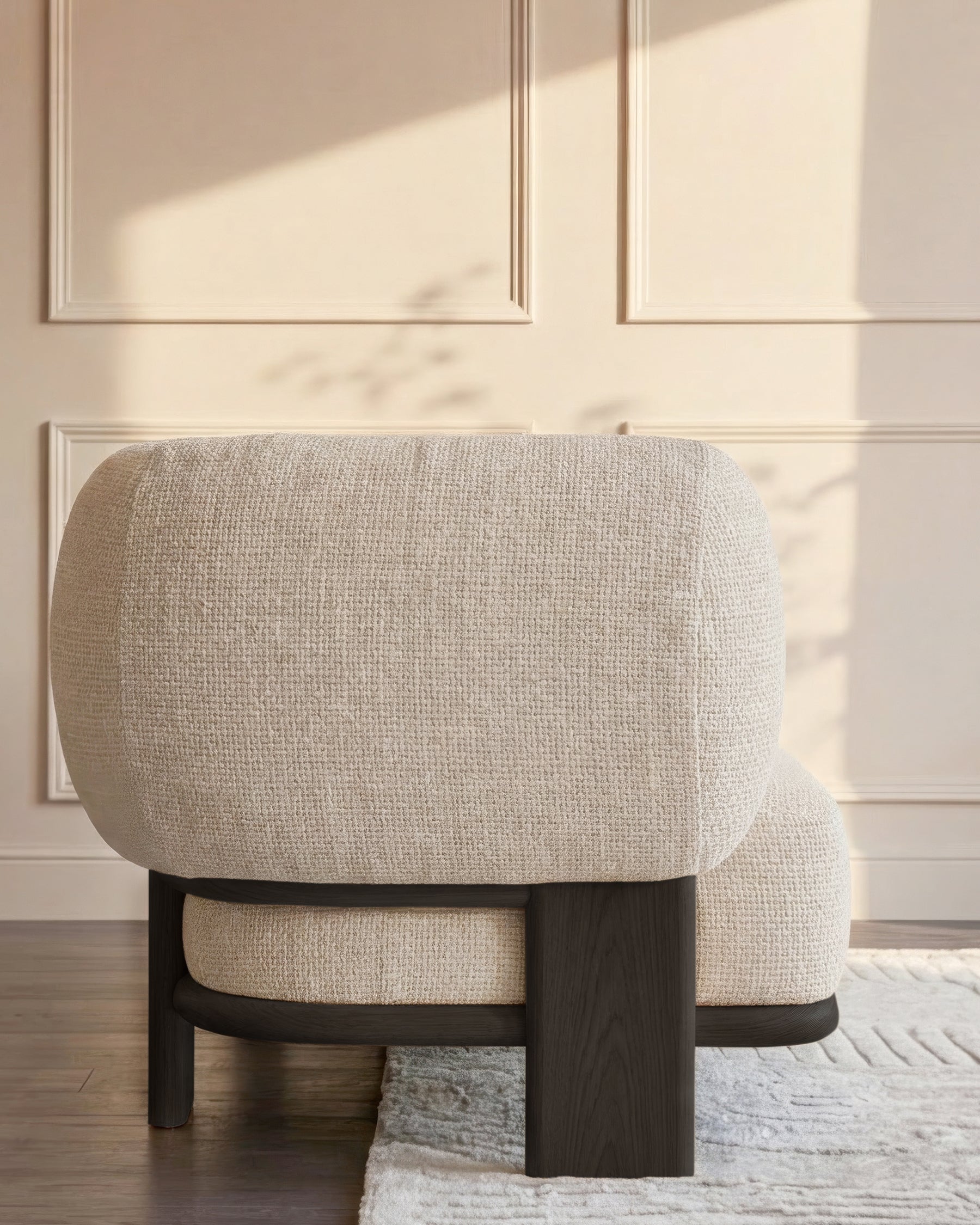 Cream upholstered armchair with curved back and dark wood frame, shown from rear angle in sunlit room.