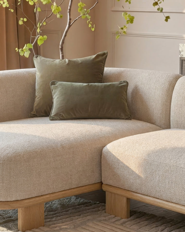 Florence left-hand facing chaise sofa in natural fabric with light wood base, styled with green pillows and decorative plant.