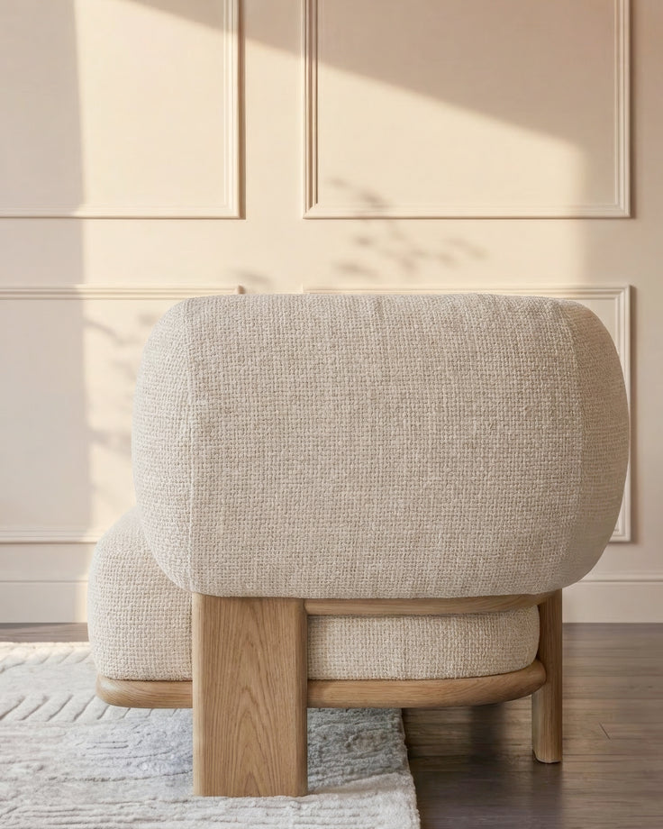 Cream upholstered chaise lounge with rounded back and natural wood frame, shown from rear angle in minimalist room.
