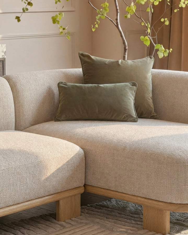 Florence right-hand-facing chaise sofa in natural fabric with light wood base, styled with olive pillows and decorative branch with foliage.