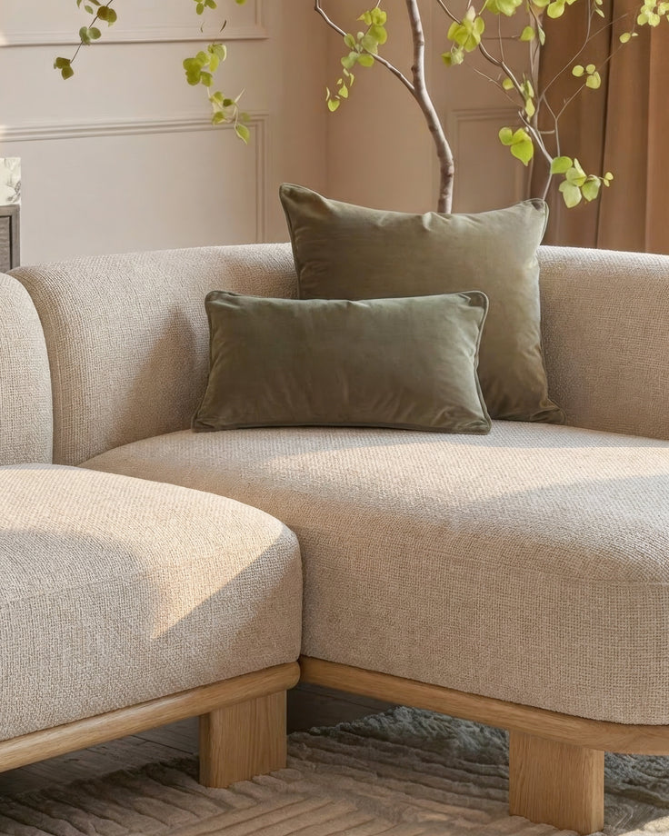 Florence right-hand-facing chaise sofa in natural fabric with light wood base, styled with olive pillows and decorative branch with foliage.