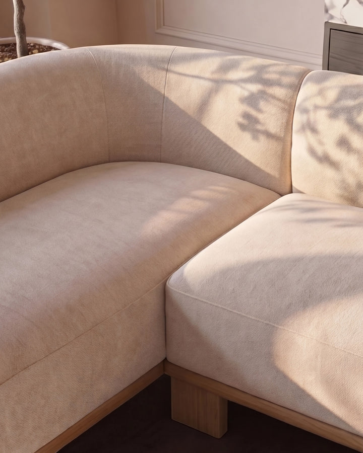 Florence left-hand corner sofa in natural fabric with light wood base, shown from angled side view in bright sunlight.