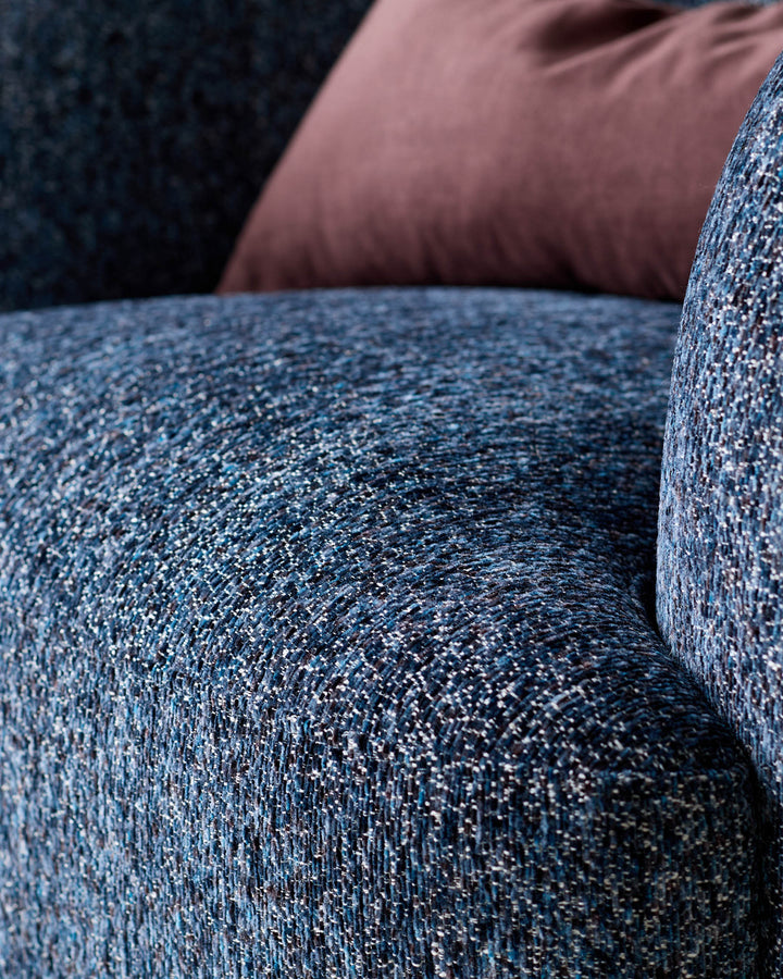 Close-up of navy weave fabric armchair showing textured upholstery detail and curved armrest edge.