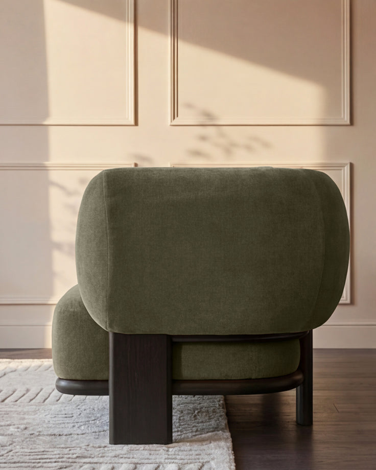 Olive green fabric corner sofa with dark wood legs, shown from side angle in minimalist room with paneled walls.