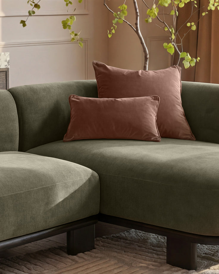 Florence right-hand-facing chaise sofa in olive-green fabric with dark wood base, styled with burgundy pillows and decorative branches.