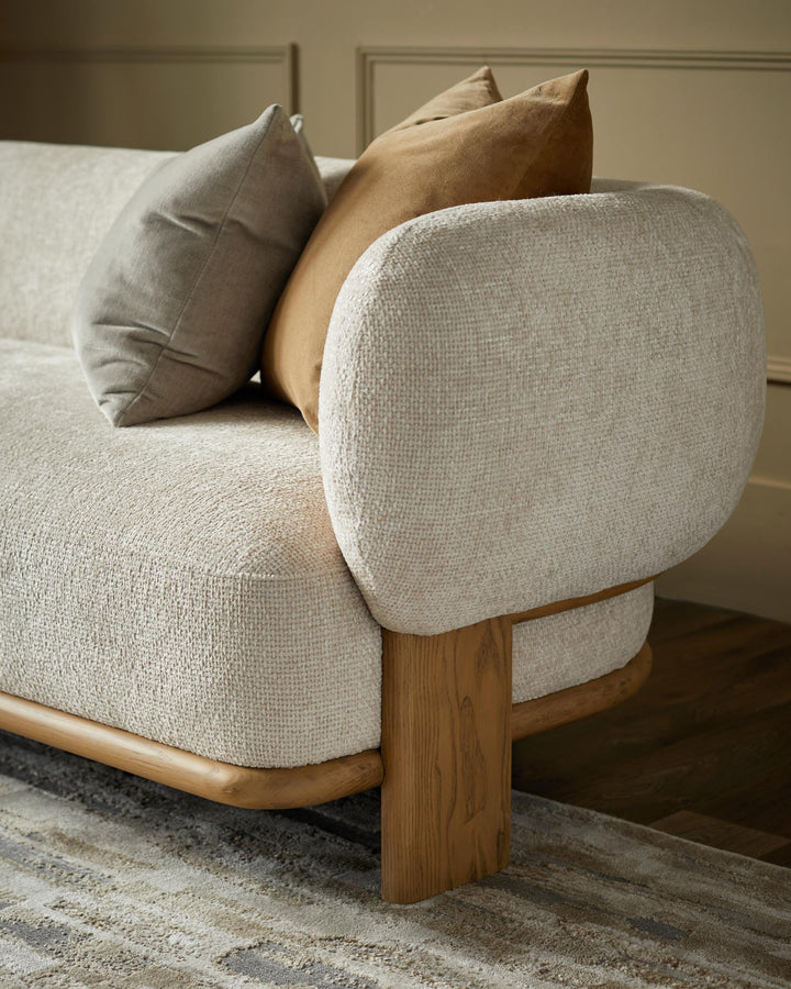 Stylish sofa with neutral cushions and a light wood frame on a patterned rug.