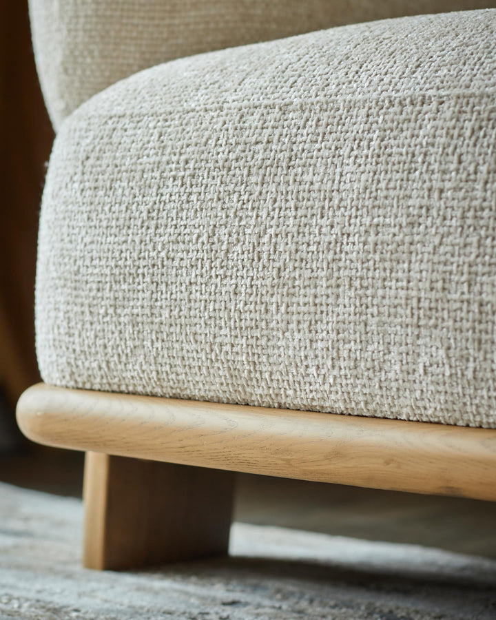 Close-up of an armchair with a light woven fabric and wooden base, showcasing texture and craftsmanship.
