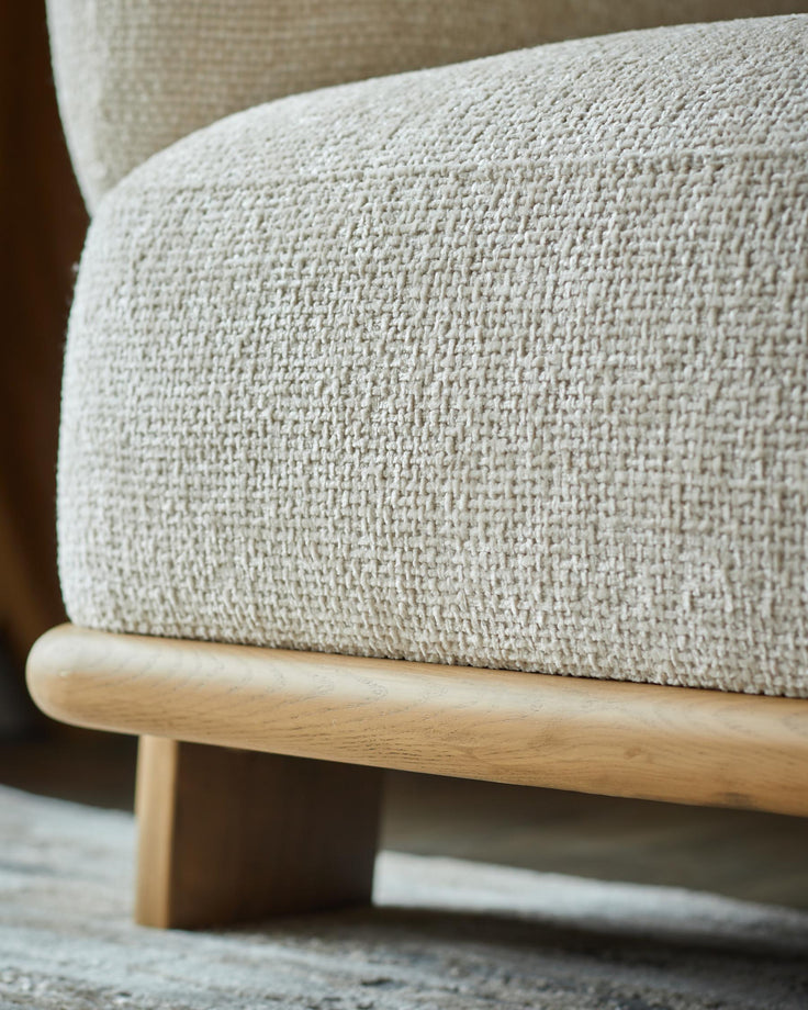 Close-up of an armchair with a light woven fabric and wooden base, showcasing texture and craftsmanship.