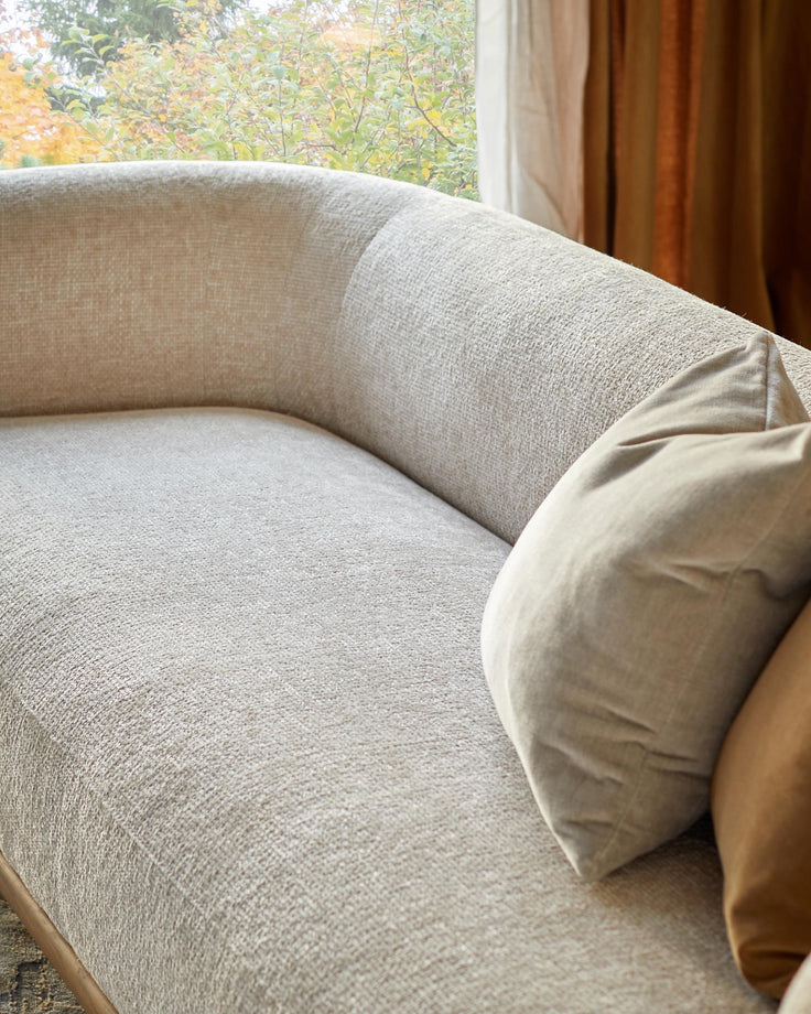A beige sofa with scatter cushions positioned near a window, offering a neutral and calming aesthetic.