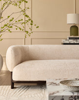 Florence 2-seater sofa in natural fabric with curved arms and dark wood legs, shown in a styled living room setting.
