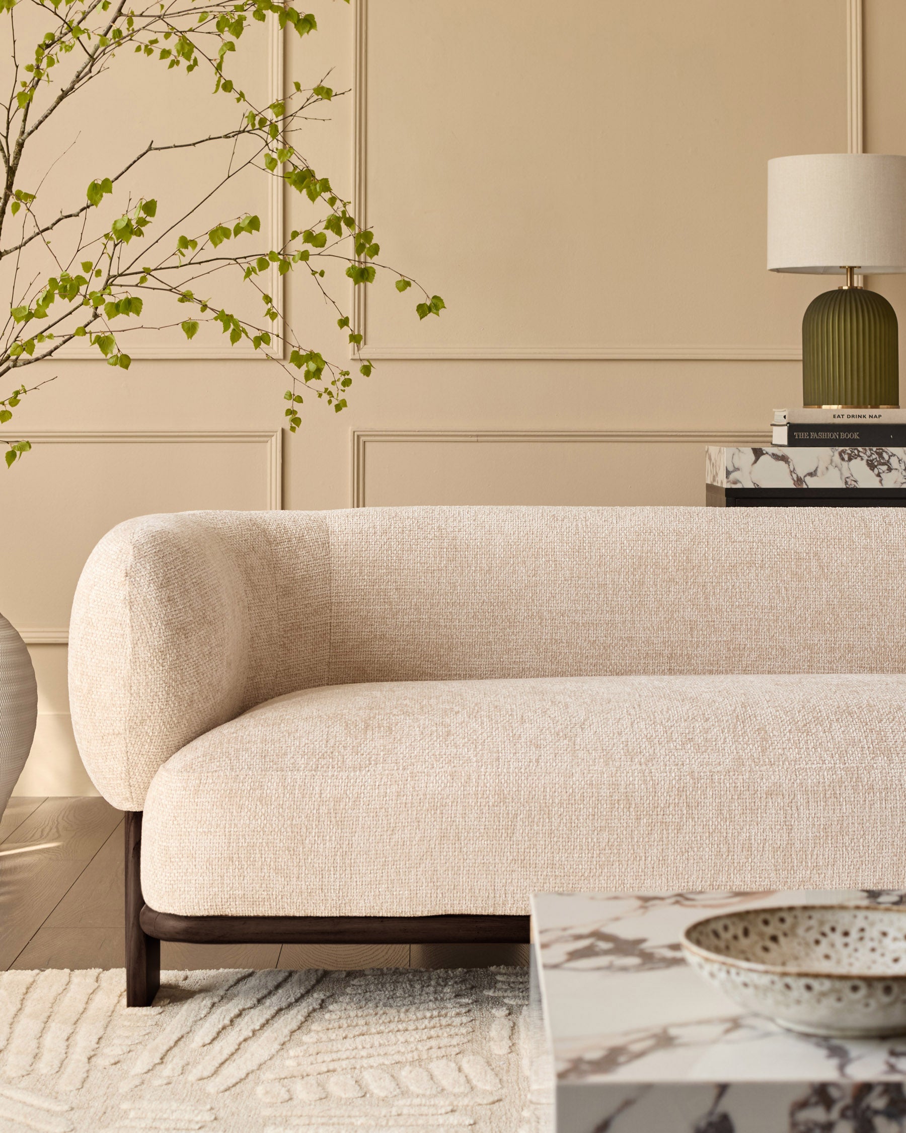Florence 2-seater sofa in natural fabric with curved arms and dark wood legs, shown in a styled living room setting.