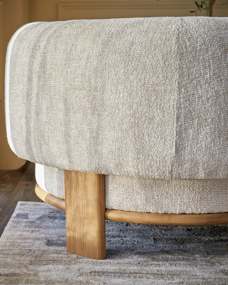Close-up of a stylish, beige, textured armchair with light wood frame and legs, sitting on a neutral coloured rug.