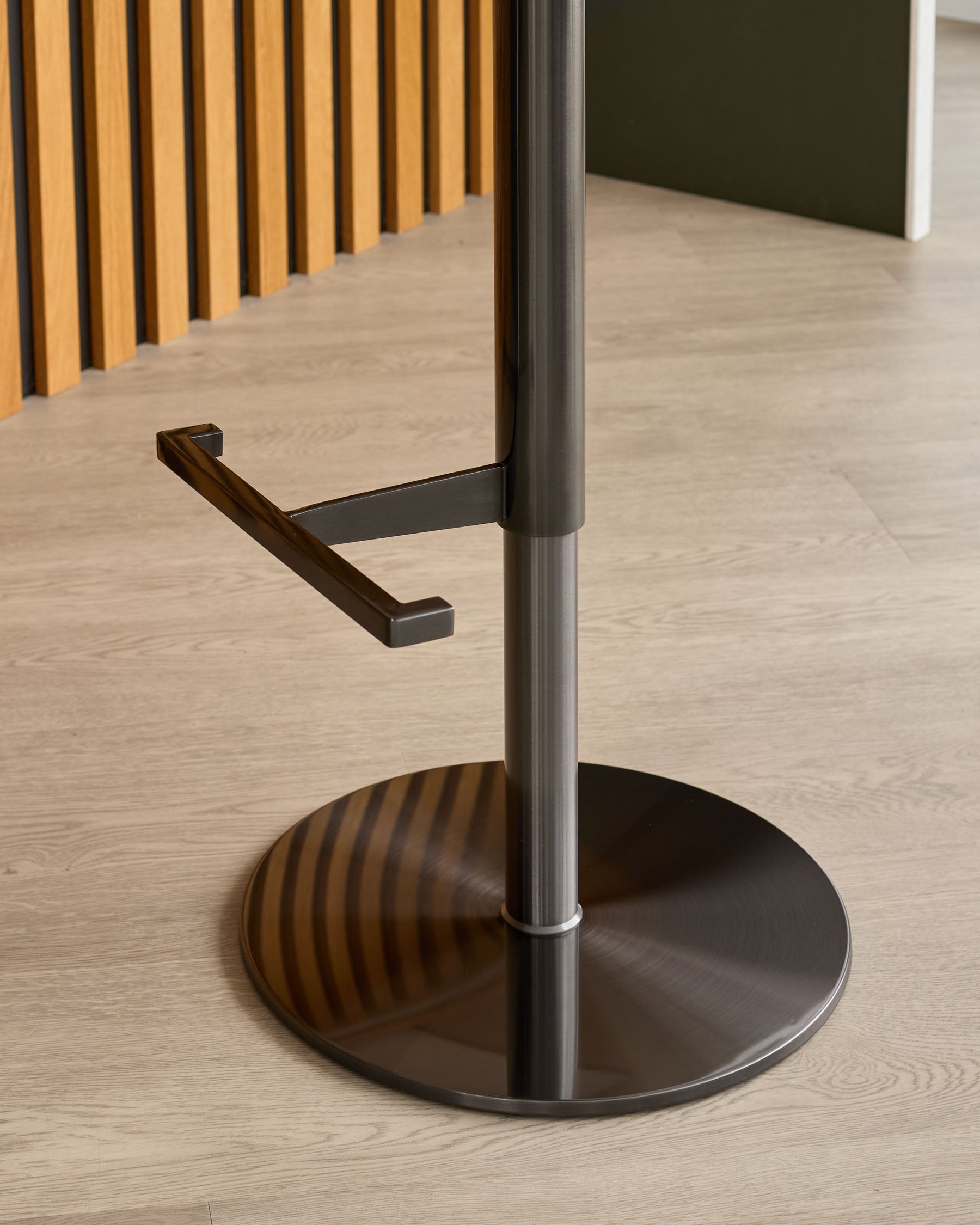 Black metal base and footrest of bar stool with dark wood handle detail, shown in interior setting.