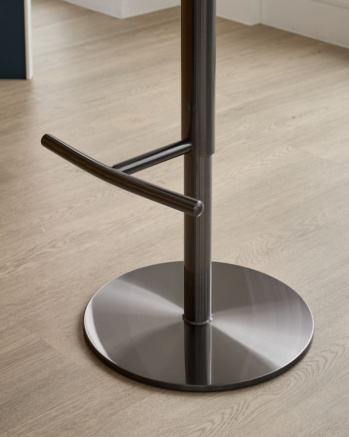 Brushed metal base and footrest of a modern bar stool with black curved armrest detail on wooden flooring.