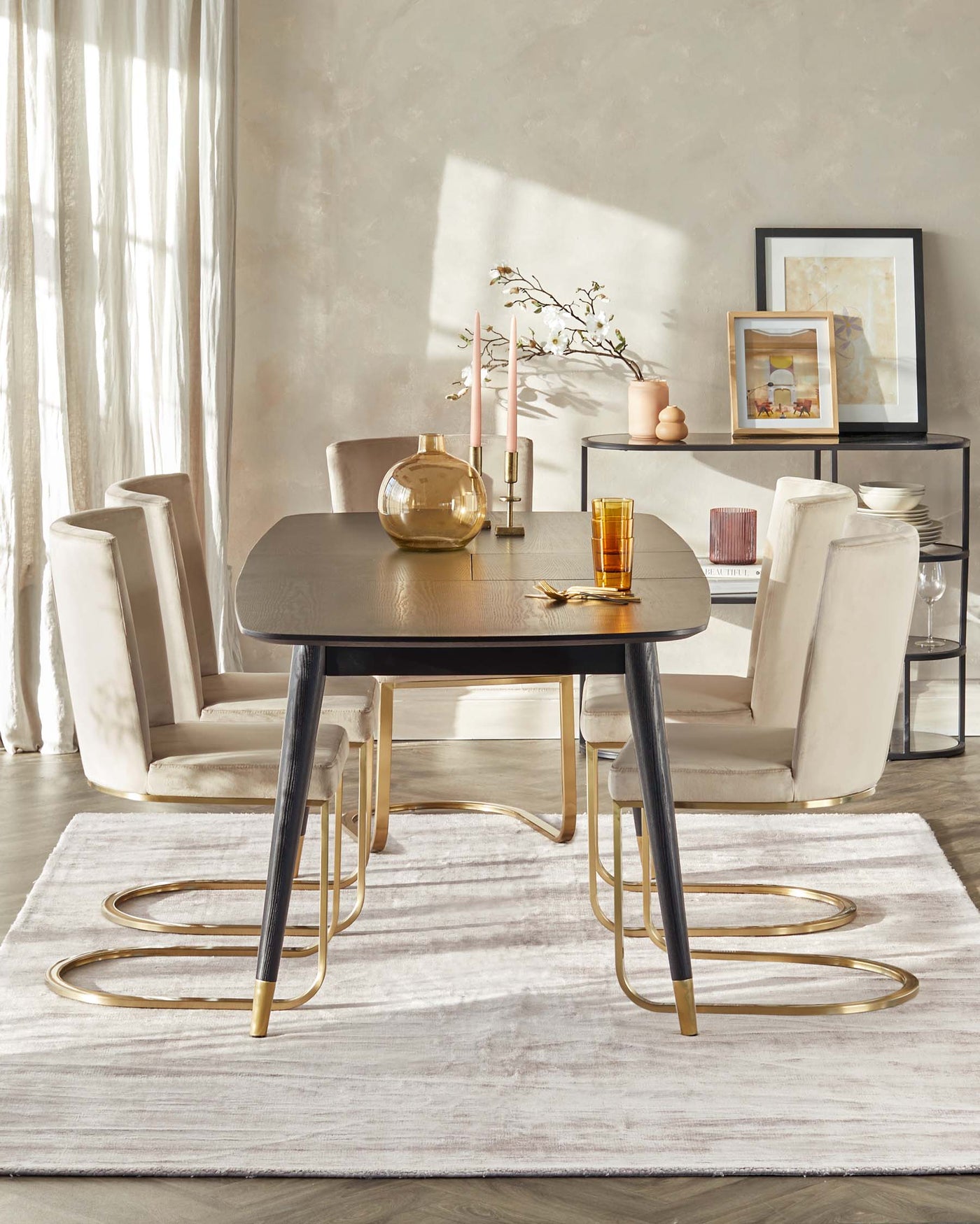 A contemporary dining room setup featuring a round, dark wood table with a fluted design and elegant brass-coloured metal legs. Four matching modern chairs with cream upholstery and brass legs are arranged around the table. The table and chairs are set on a white textured area rug. A coordinating console table with a metal frame and a glass top displays decorative items and is placed against the wall.