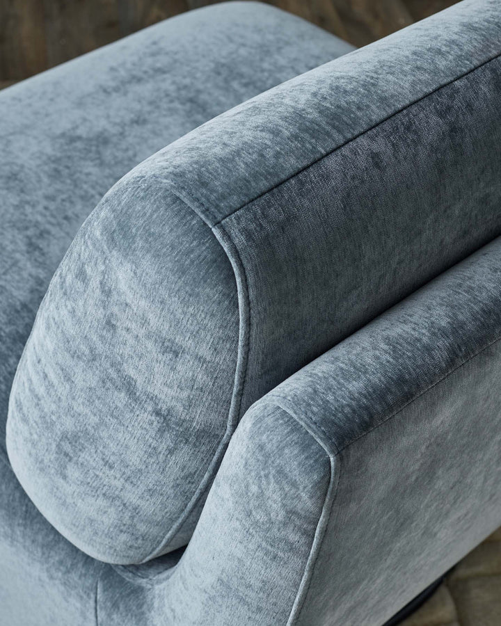 Close-up of a modern chair with a plush, textured light blue fabric, showcasing its curved armrest design.