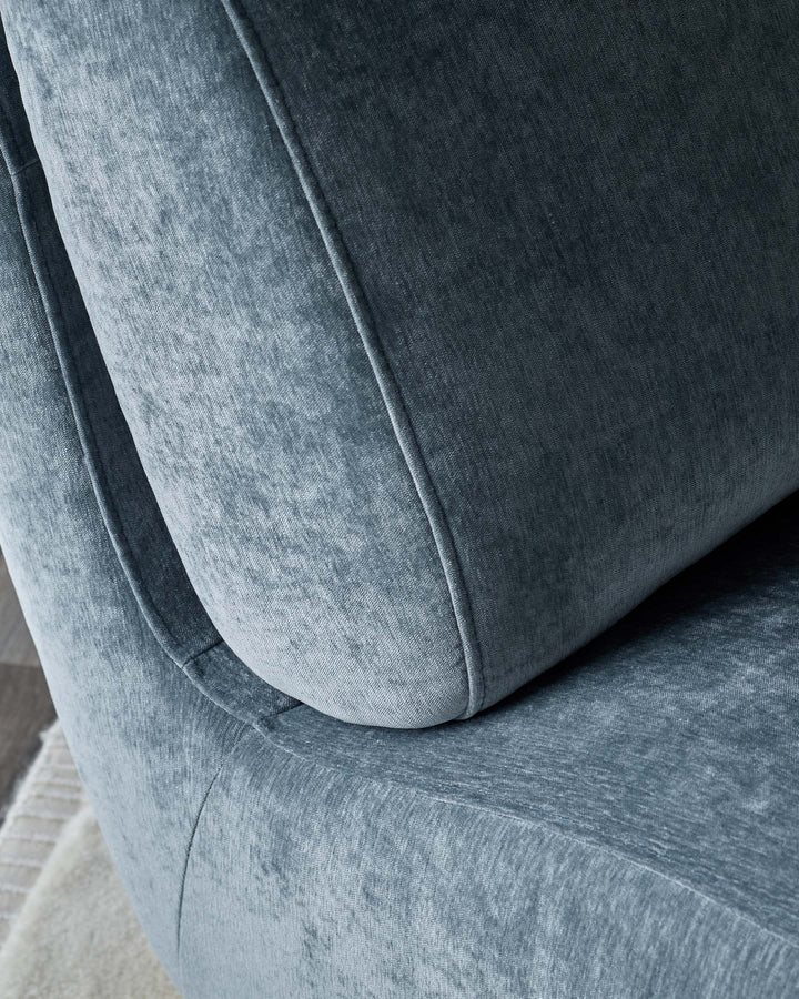 Close-up of a stylish, blue-grey velvet armchair with a rounded back and plush cushioning.