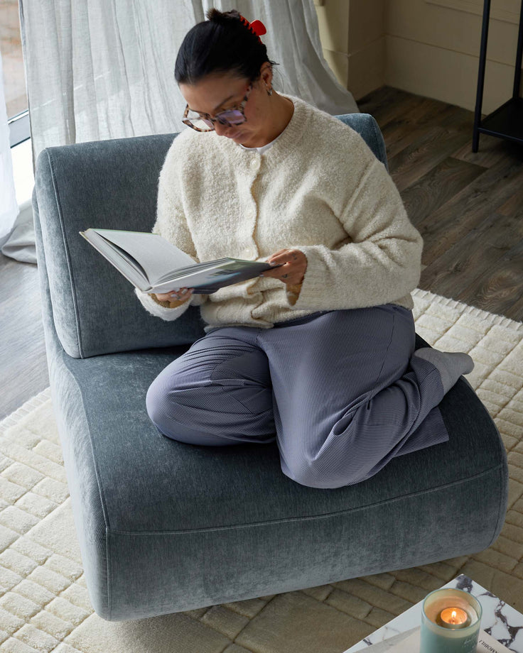 Upholstered lounge chair with grey material, paired with a textured rug, offering a cosy seating experience.