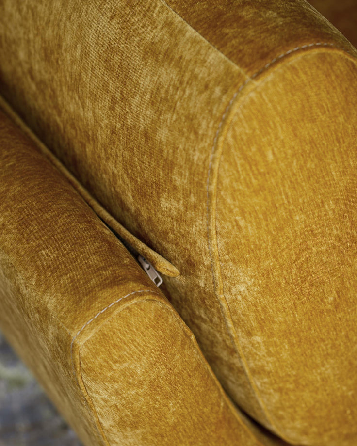 Close-up of a mustard yellow upholstered chair with stitching and a zipper detail, offering a textured and inviting look.