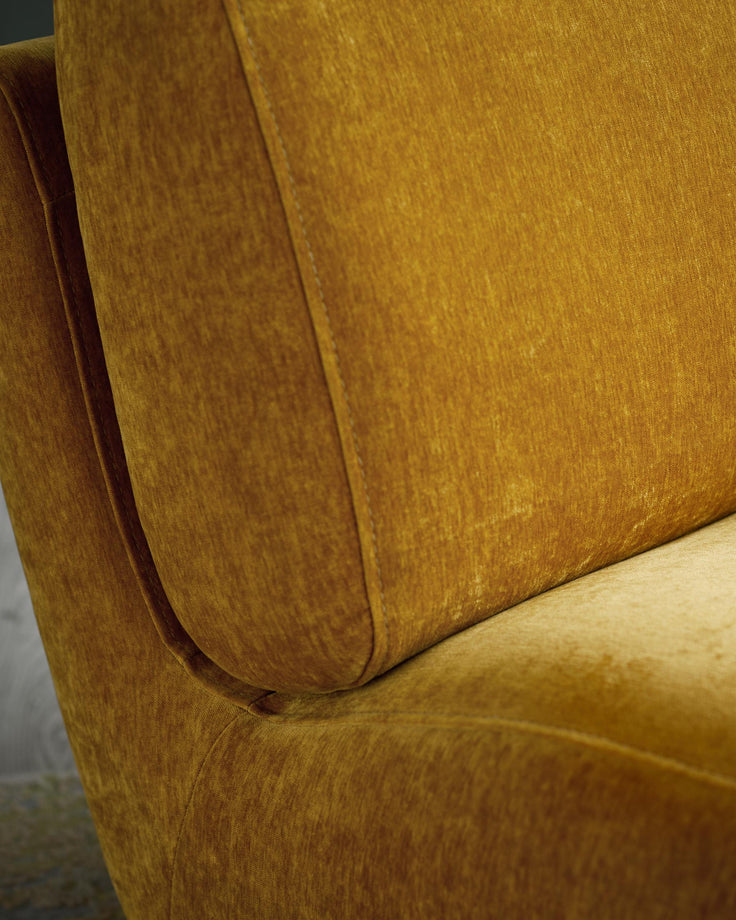 Close up of a mustard coloured armchair with button detailing. The material has a soft, velvet texture.
