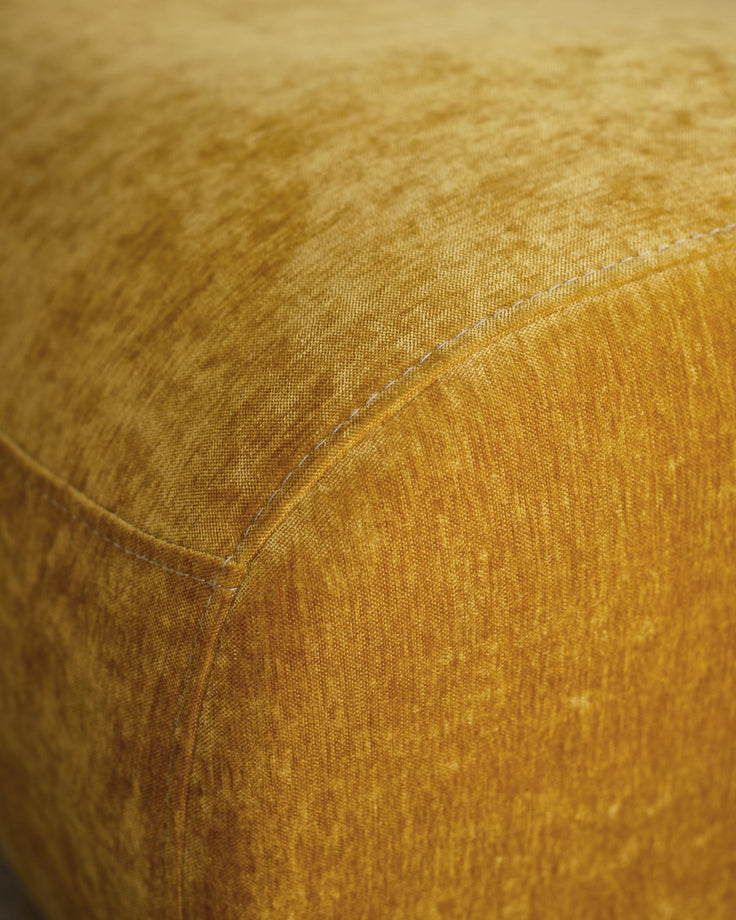 Close-up of a mustard-yellow pouffe with visible stitch detailing, showcasing its textured fabric and design.