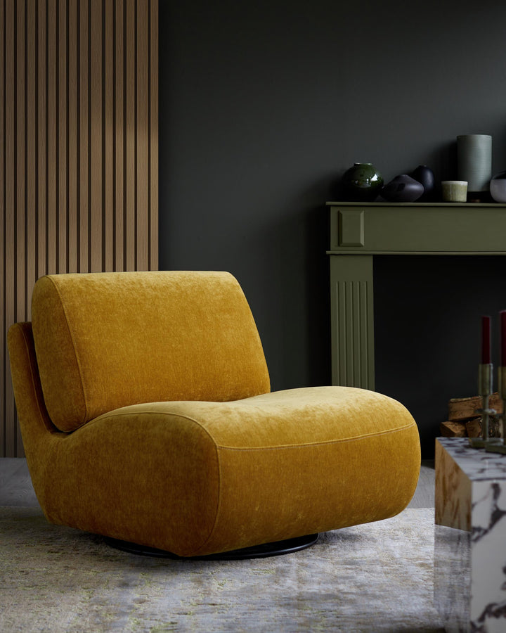 A mustard velvet swivel armchair sits on a patterned rug in front of a dark green wall and wooden panelling.