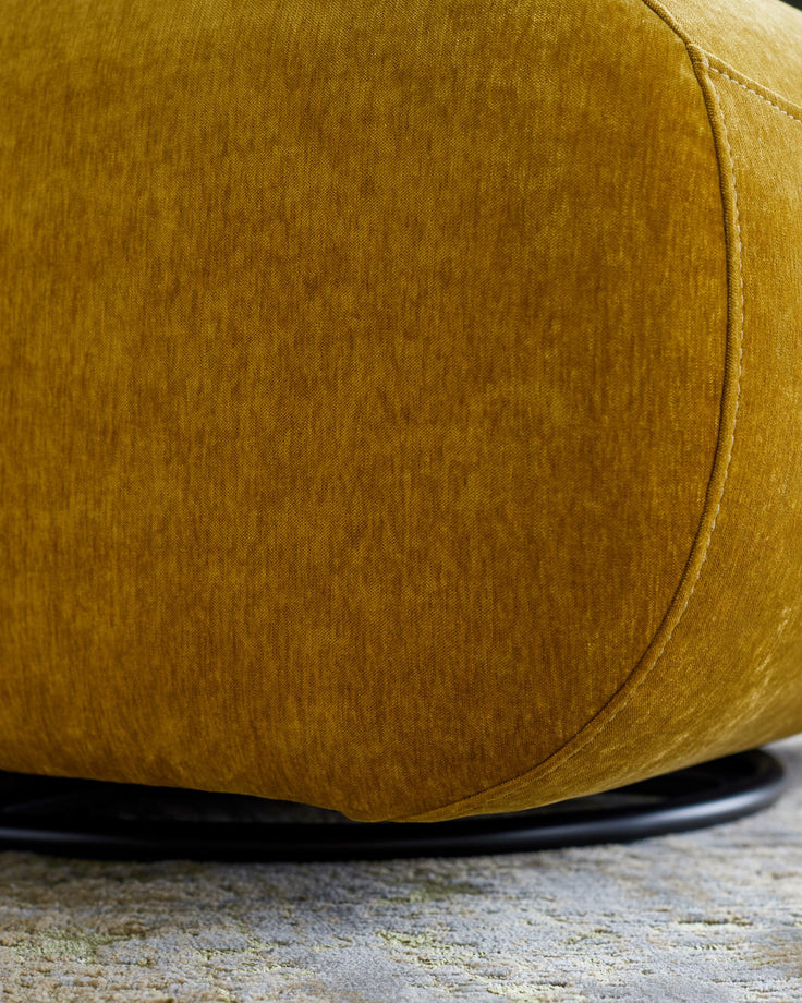 Close-up of an ochre velvet ottoman, showcasing its texture and design on a patterned rug.