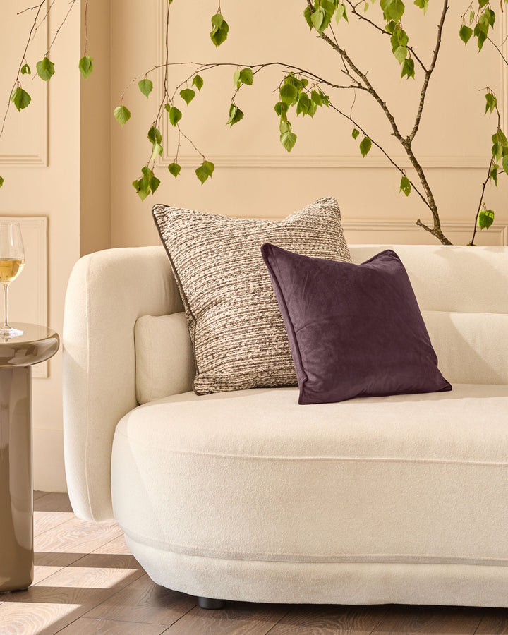 Franco cushion in large size, chocolate brown velvet, displayed on a cream armchair in a styled living room setting.