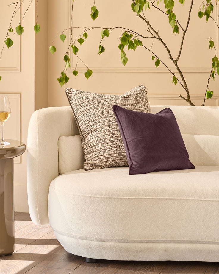 Franco cushion in large size, chocolate brown velvet, displayed on a cream armchair in a styled living room setting.