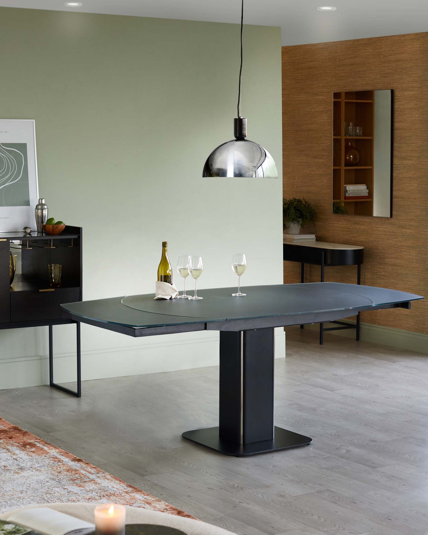 Modern dining room featuring an elegant rectangular black dining table with a sleek pedestal base, paired with a matching sideboard in the background, and a stylish metallic pendant light hanging above.