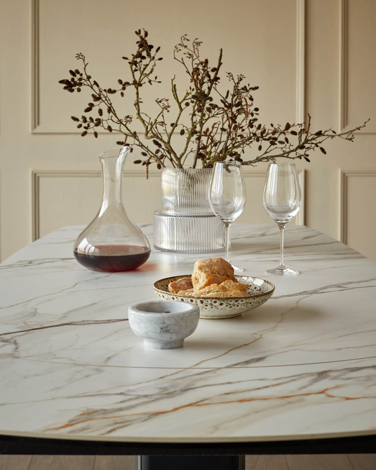 Table setting with wine, bread, and glasses on a marble-patterned table, complemented by a decorative floral arrangement.