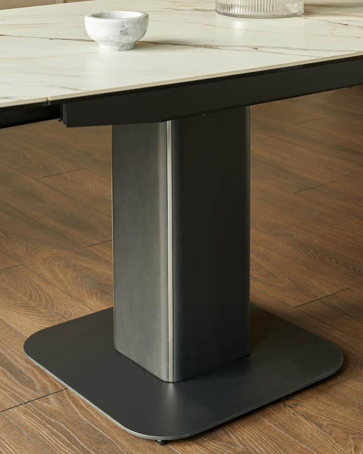 A modern dining table with a marble top and a dark metal base, standing on a wooden floor.