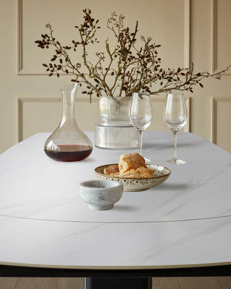 White marble-effect round dining table styled with wine decanter, glasses, dried flowers, and bread bowl.