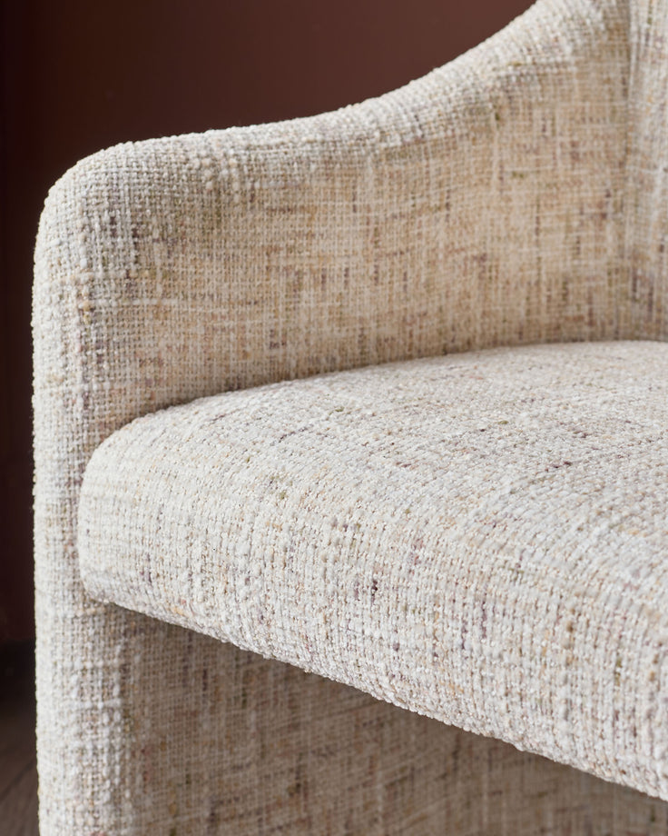 Freya dining chair in natural fabric, close-up of textured weave showing curved backrest and seat detail against brown background.